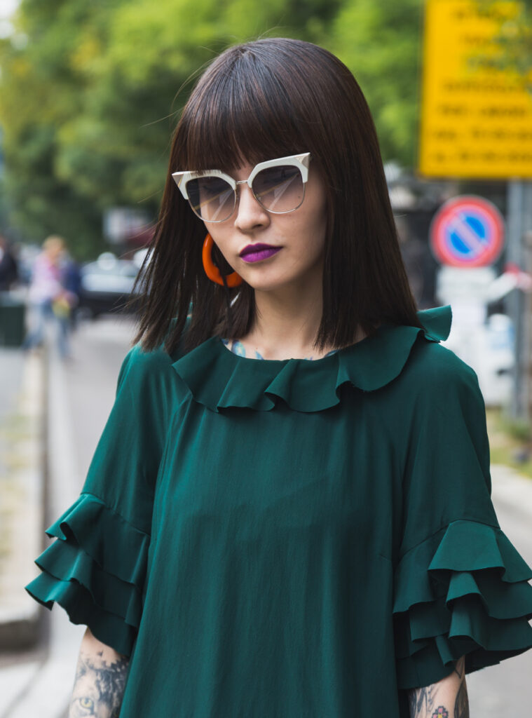 Woman wearing a dark green dress with layered ruffle sleeves and bold sunglasses